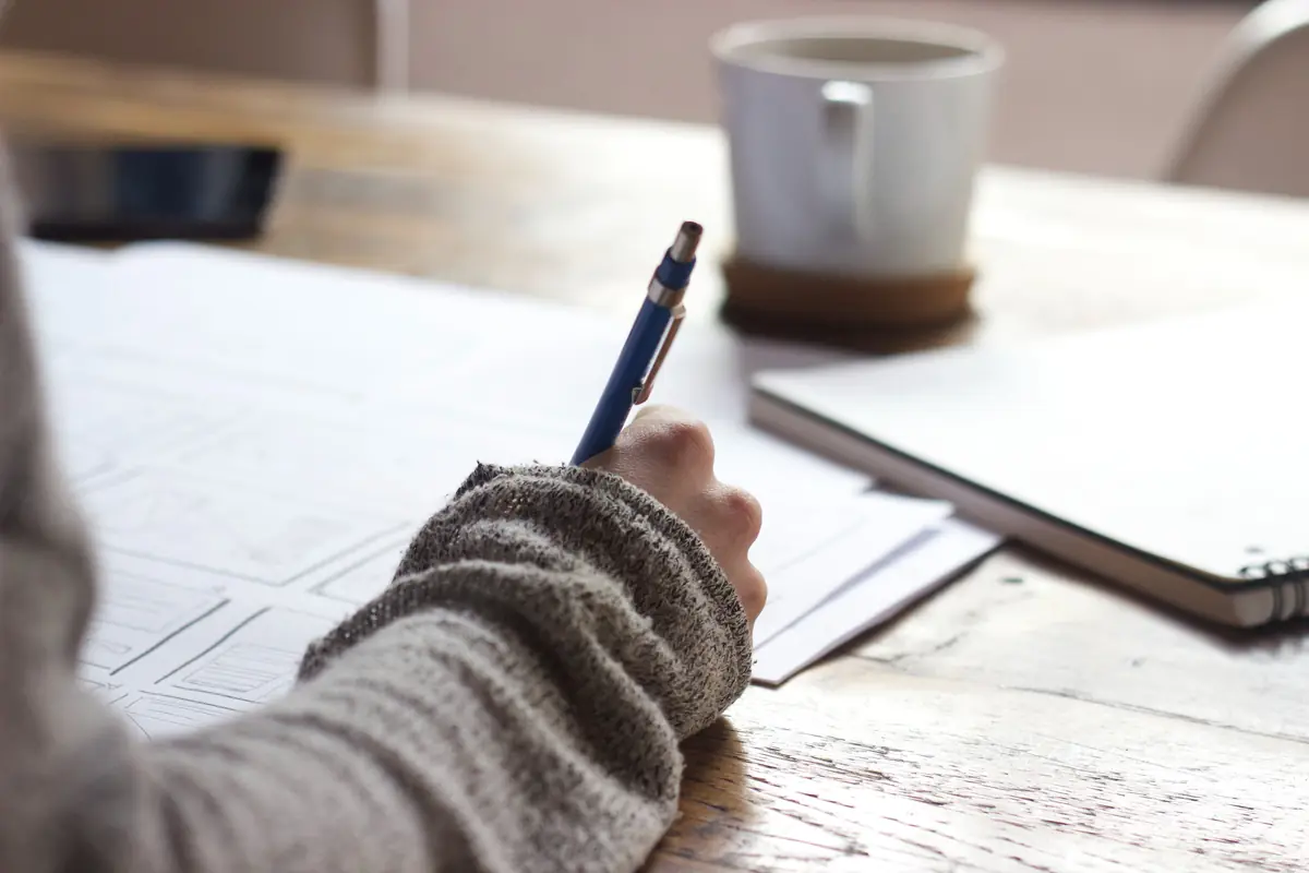 Person writing notes at a desk next to a coffee mug